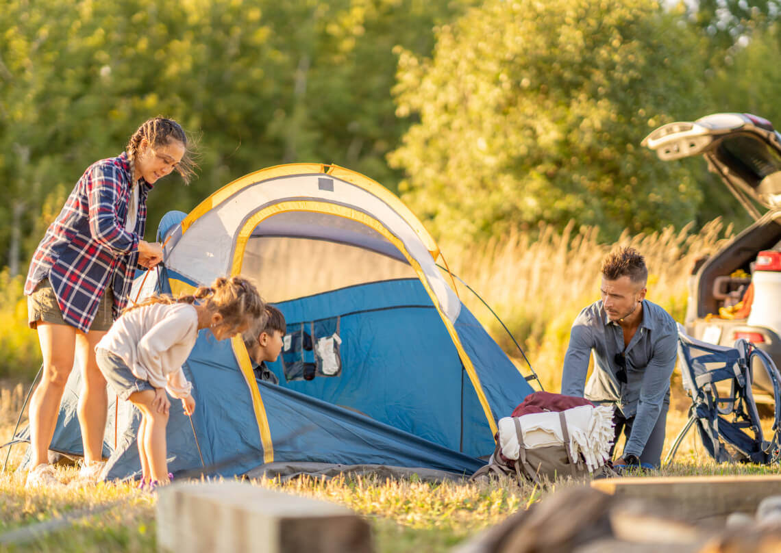 A family setting up a blue and yellow tent in a grassy field.